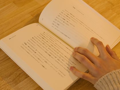 机の上で本を開き、左手で押さえてながら読んでいる